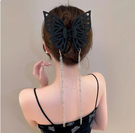 Black butterfly hair accessory with dangling beads on a person's bun against a neutral background