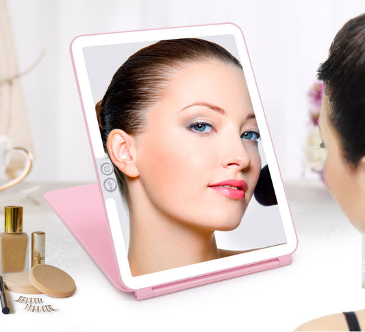 Woman using a pink handheld mirror with a lighted surface to check her makeup.