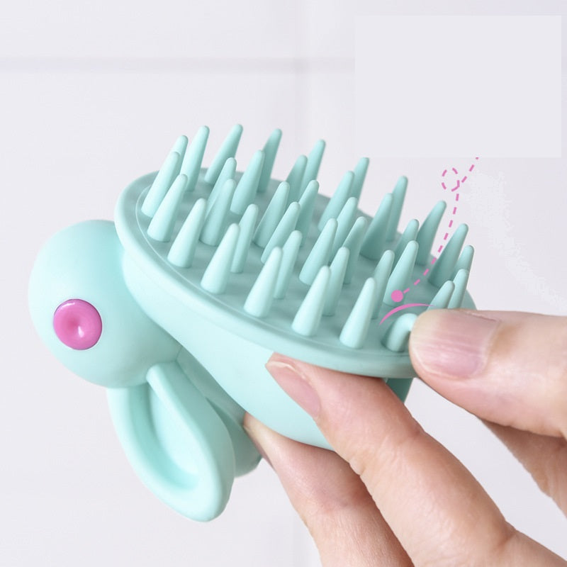 Light blue silicone scalp massager with pink button held by a hand on a light background